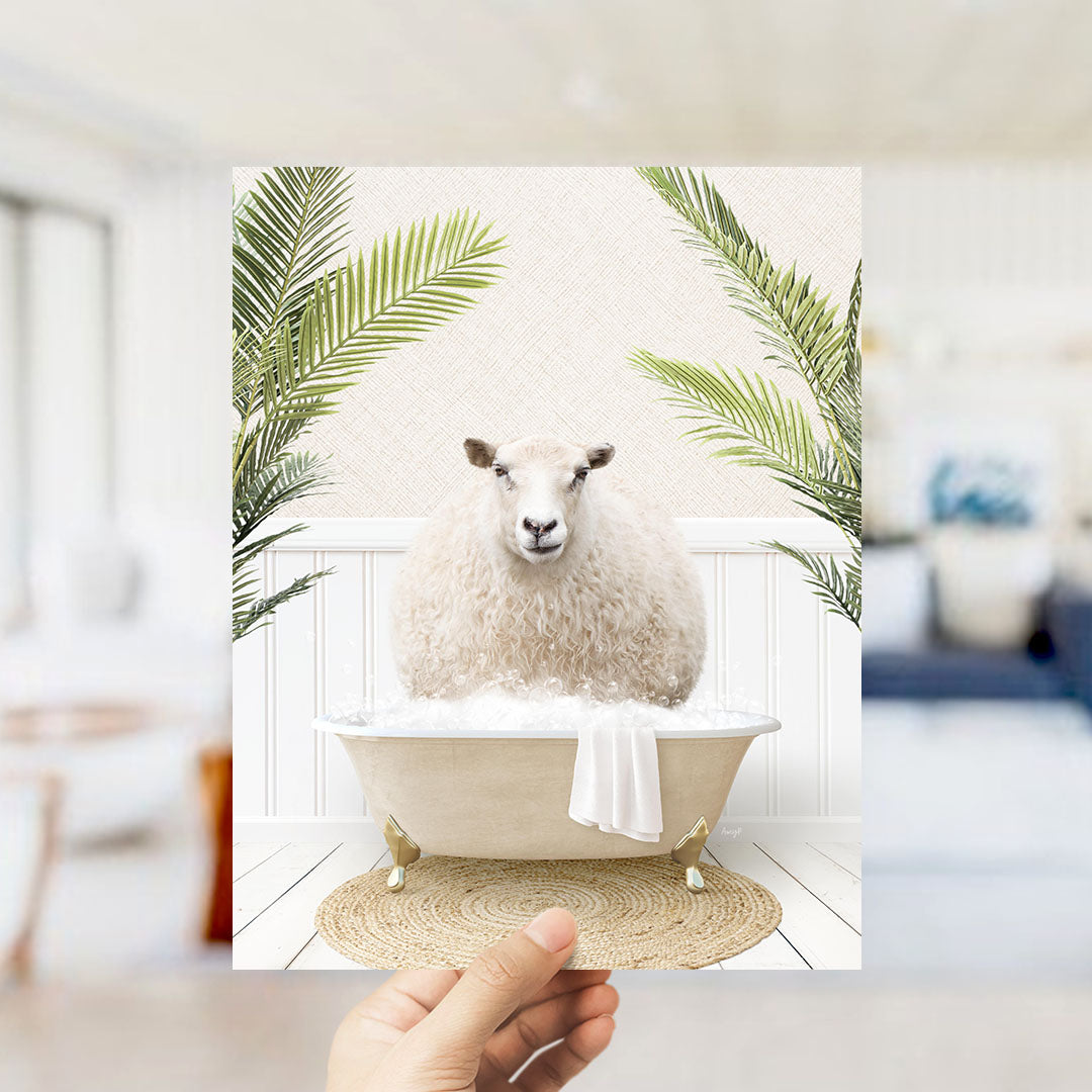 A hand holds up a framed image depicting a sheep sitting in a bathtub filled with bubbles, surrounded by green palm leaves.