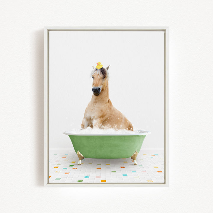 A light brown horse is sitting in a green bathtub filled with bubbles, wearing a yellow rubber duck on its head.