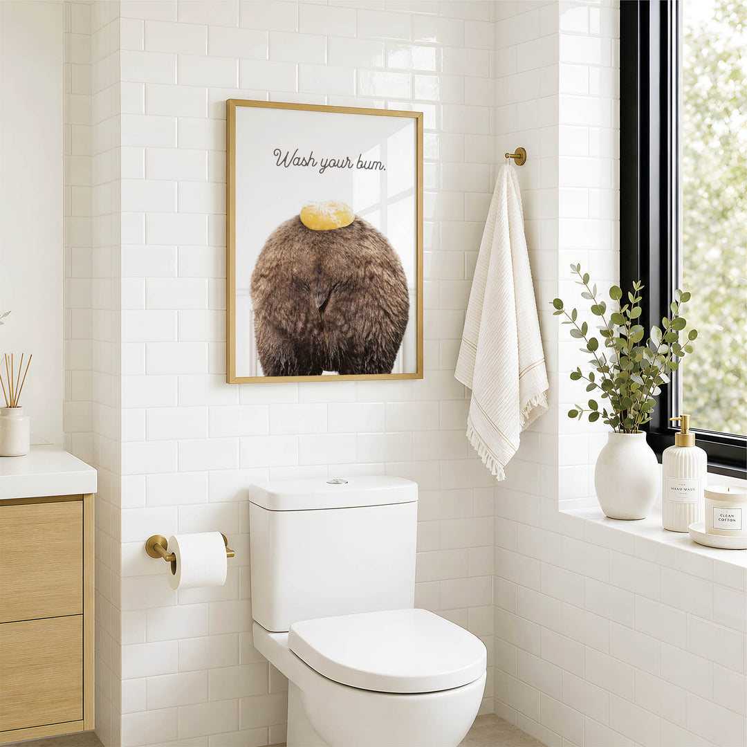 a bathroom with a white toilet, a framed poster with a brown animal on top of it, and a window with a plant on the sill.