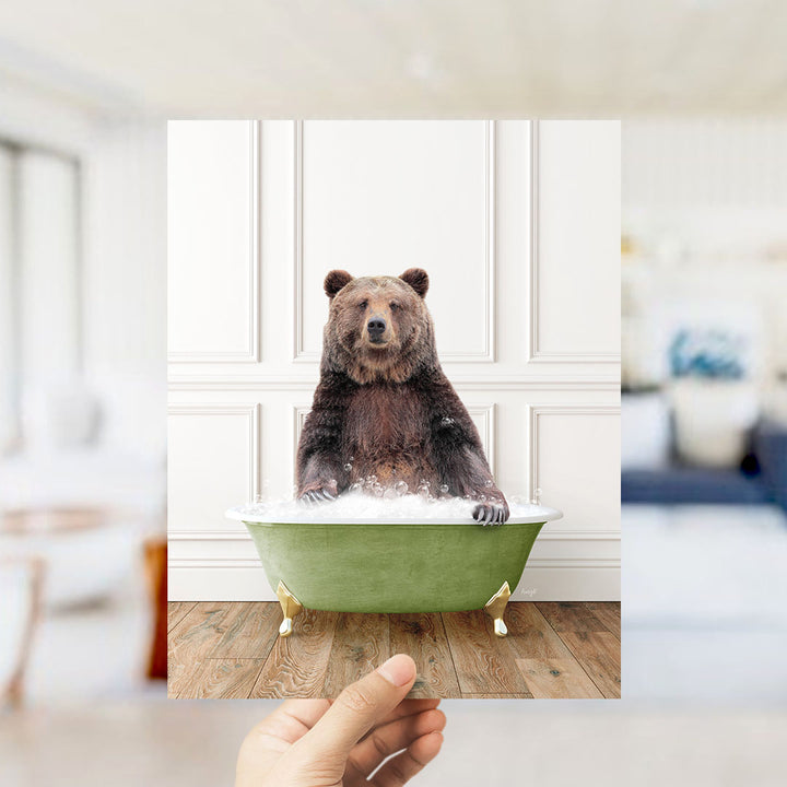 A hand holds up a photo of a brown bear sitting in a green bathtub filled with water, creating a whimsical and playful scene.