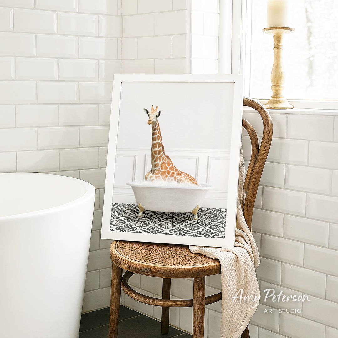 A framed image of a giraffe sitting in a bathtub is displayed on a wooden chair in a bathroom setting.
