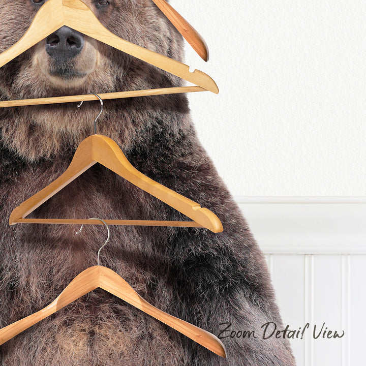 A large brown bear is standing in front of a white wall, with several wooden hangers hanging from its mouth and neck.