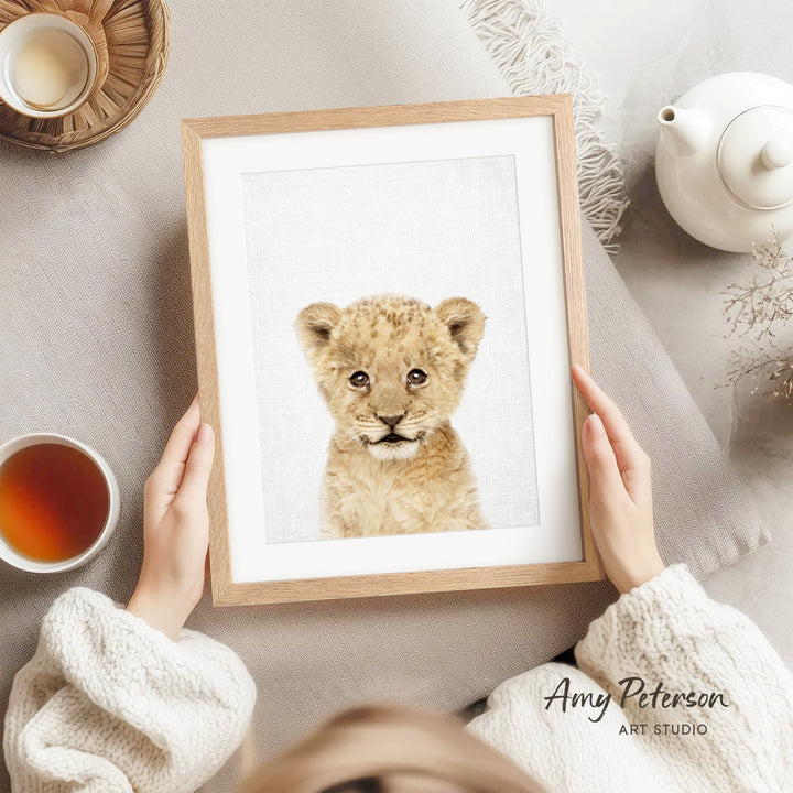 A person is holding a framed picture of a young lion cub, which is the main focus of the image.