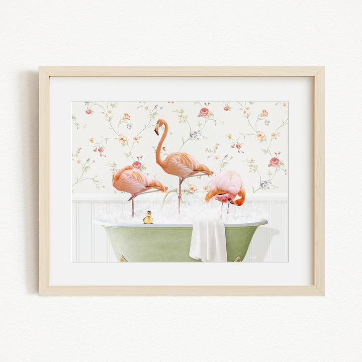 A framed image depicting three pink flamingos standing in a green bathtub filled with water, surrounded by a floral patterned wall.