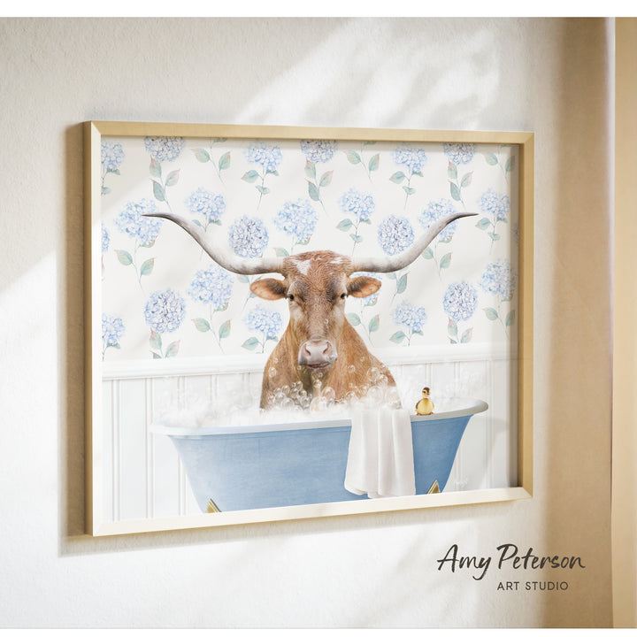 A framed print of a bull with large horns sitting in a blue bathtub filled with bubbles, surrounded by a floral pattern.