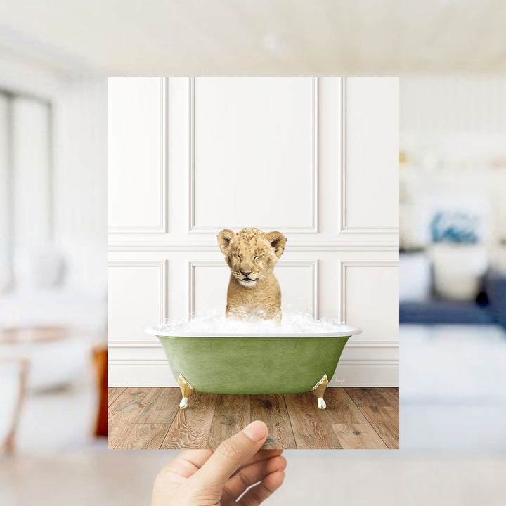 A young lion cub sitting in a green bathtub filled with water, with a blurred background suggesting a living room setting.