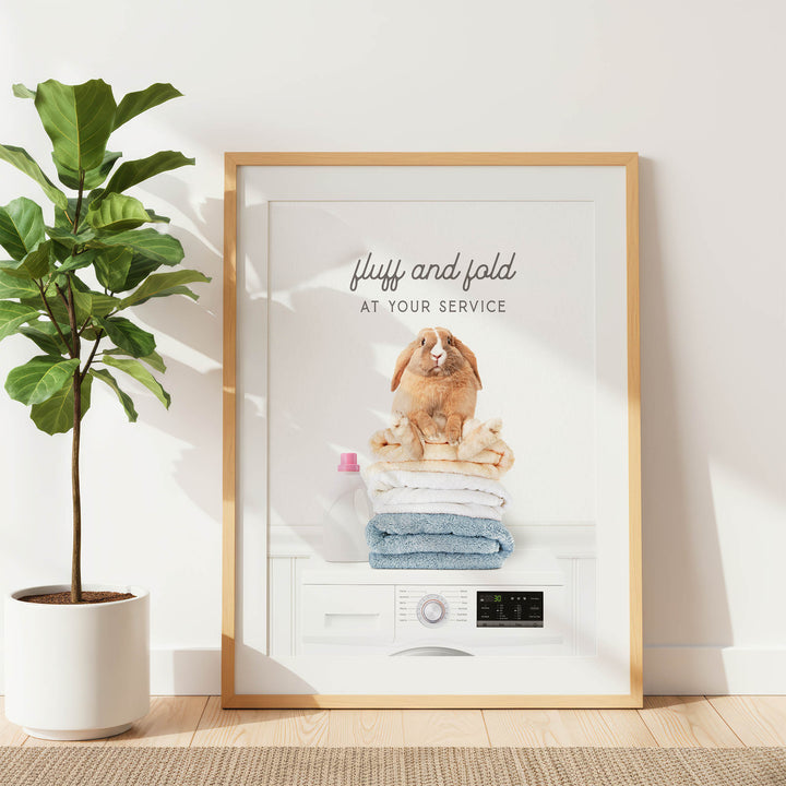 a framed poster with a rabbit sitting on top of folded towels, accompanied by the text "fluff and fold at your service".