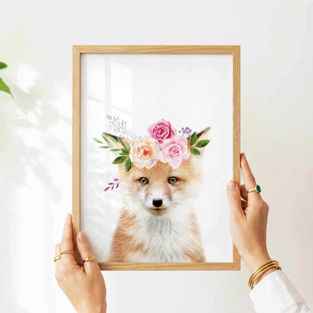 A person's hands are holding a framed picture of a fox wearing a floral crown.