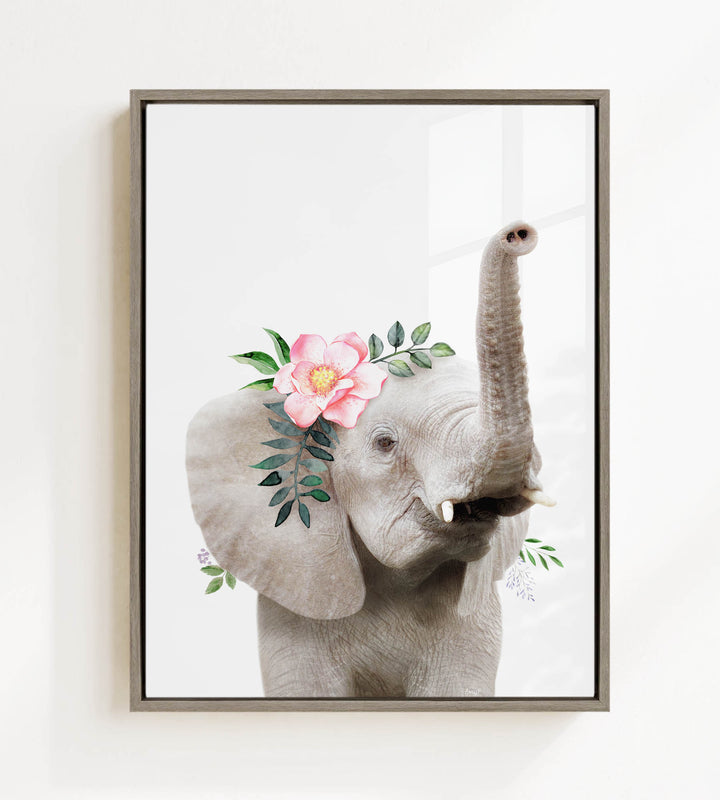 A framed image of an elephant with a pink flower and green leaves adorning its head.