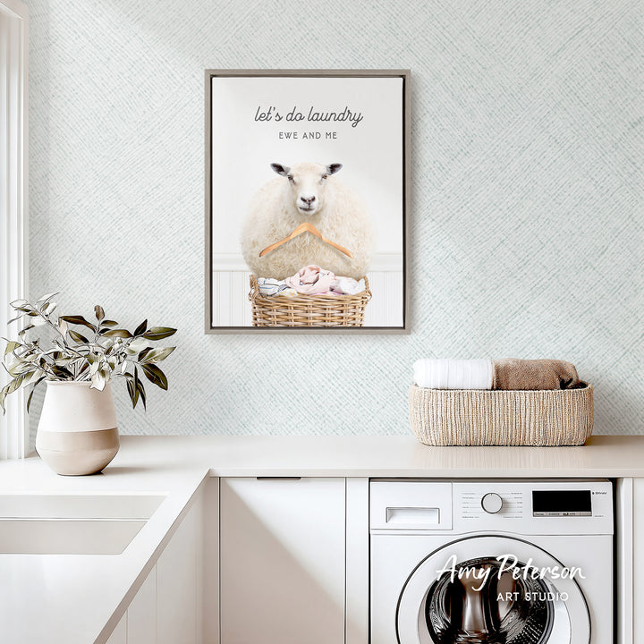 a framed poster of a sheep hanging on a wall above a laundry basket, which is placed on a white countertop.
