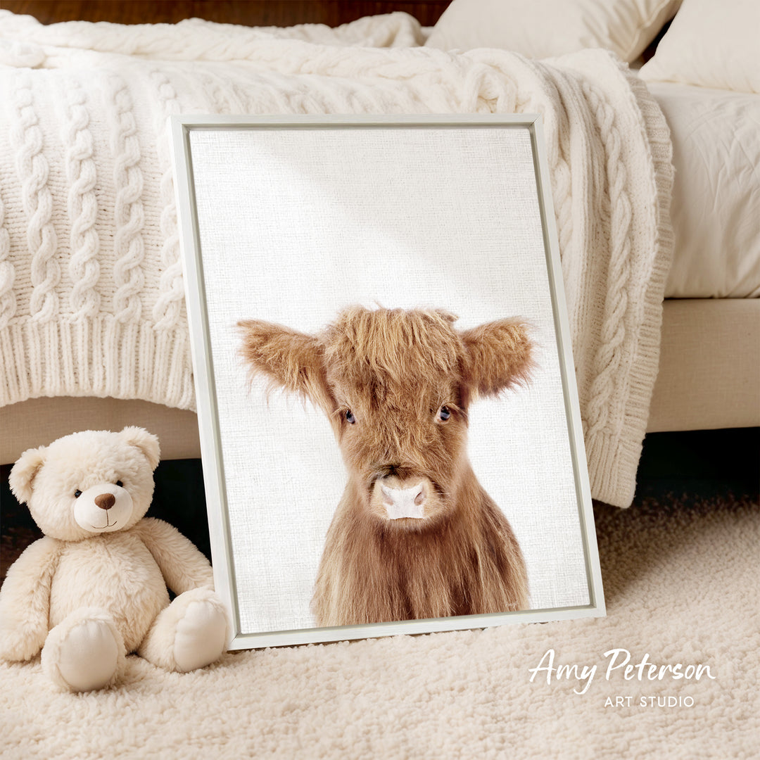 A framed image of a brown cow is displayed on a bed, accompanied by a teddy bear.