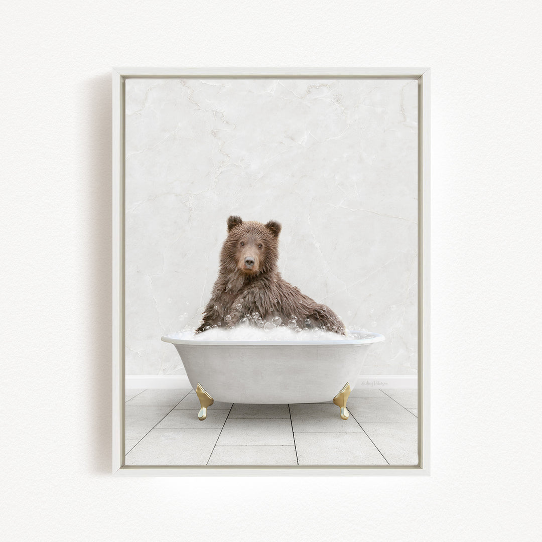 A brown bear sitting in a white bathtub filled with bubbles, looking directly at the camera.