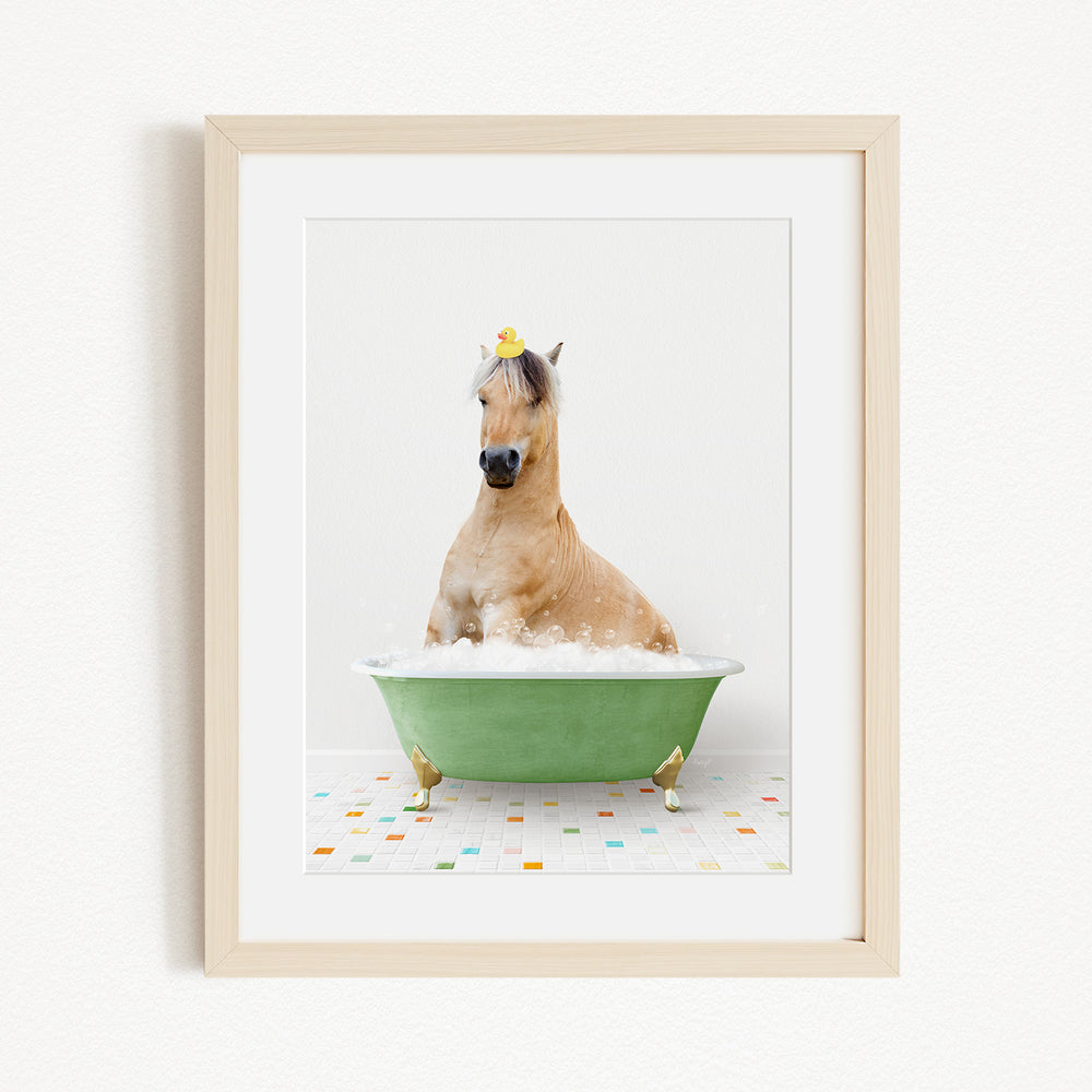 A light brown horse is sitting in a green bathtub filled with bubbles, with a yellow rubber duck perched on its head.