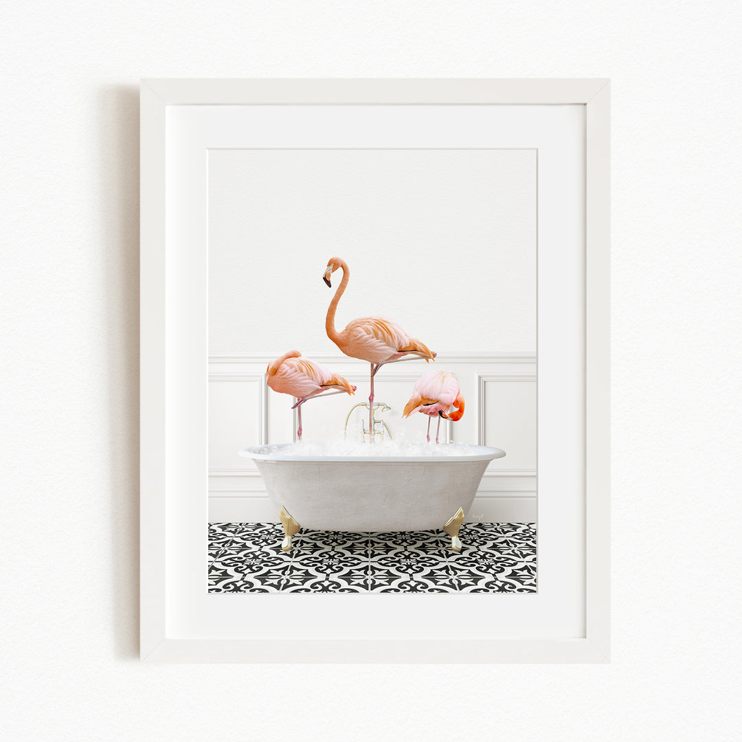 A framed image depicting three pink flamingos standing in a white bathtub filled with water, set against a black and white patterned floor.