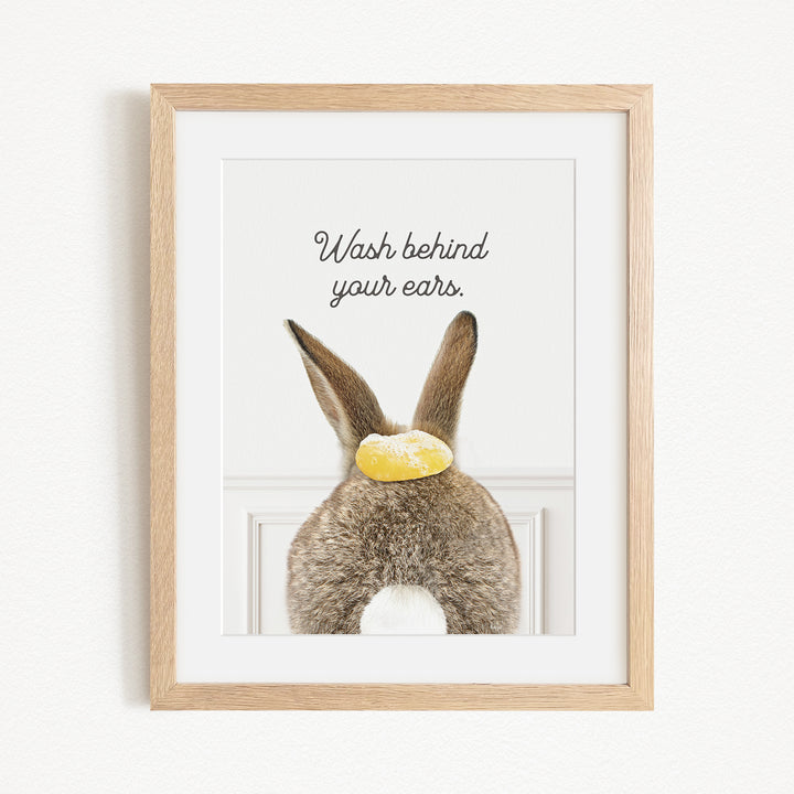 A framed image of a rabbit's back with the text "Wash behind your ears" written above it.