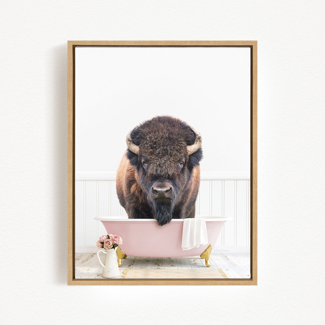 A buffalo with large horns is sitting in a pink bathtub, surrounded by pink flowers and a white vase.