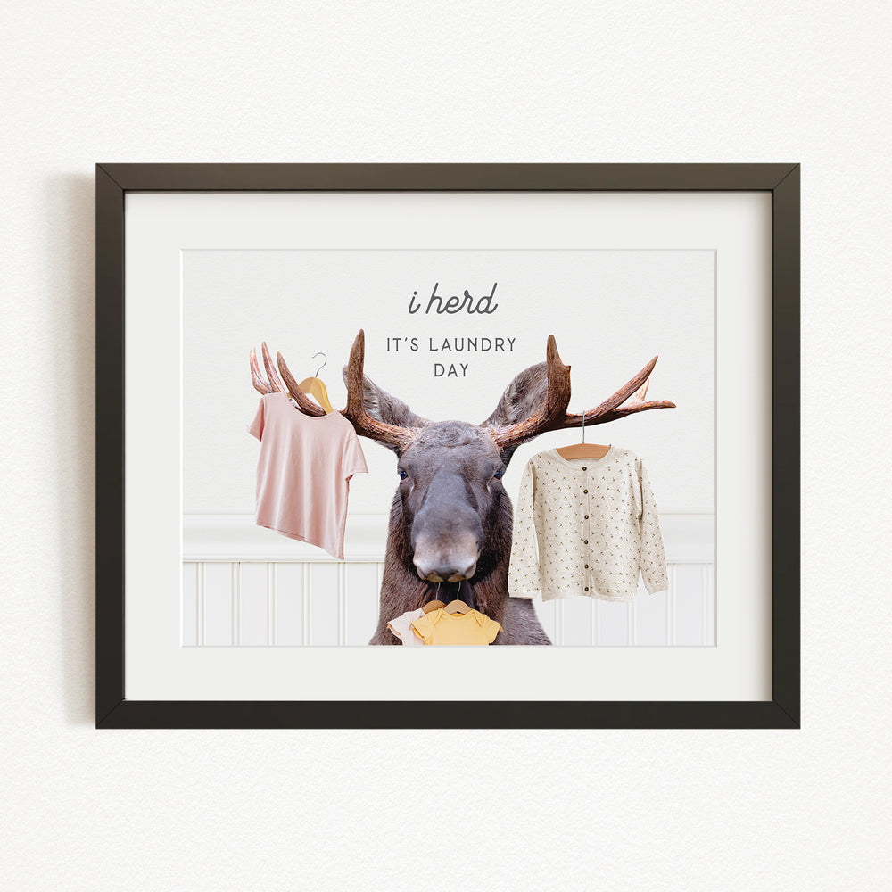 A framed collage of a moose with antlers holding clothes, accompanied by the text "It's laundry day"