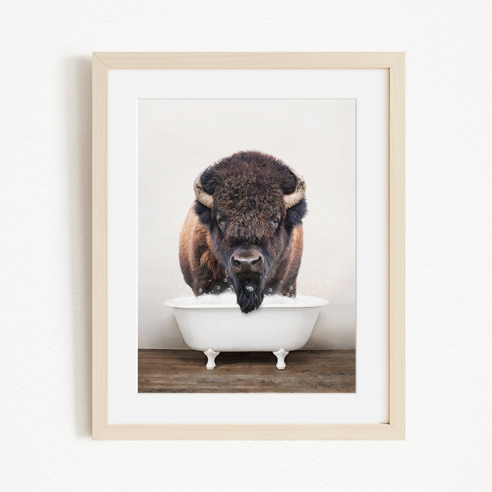 A buffalo with large horns is standing in a white bathtub, appearing to be enjoying a bath.