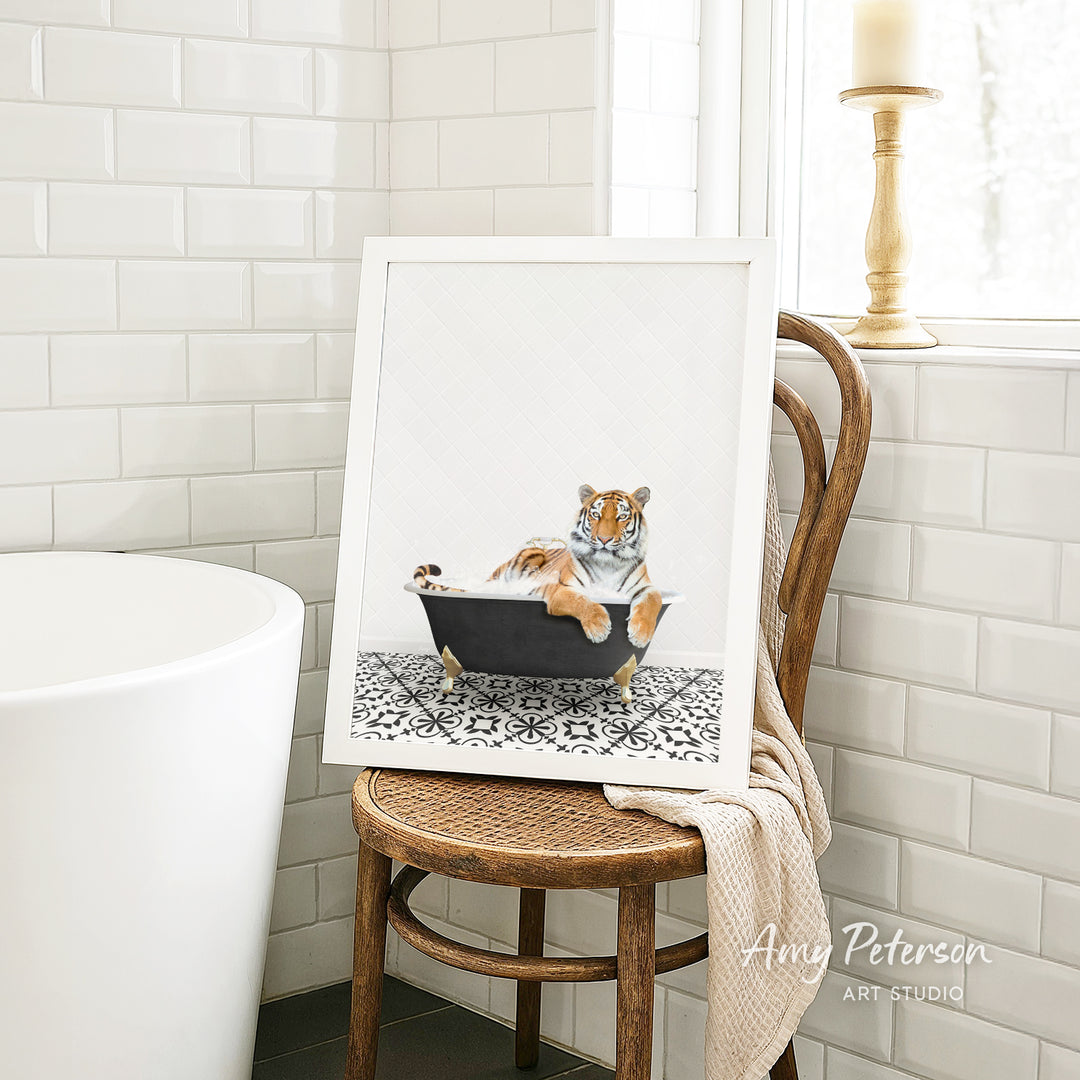 A framed image of a tiger sitting in a bathtub, with a towel draped over the back of a chair in a bathroom setting.