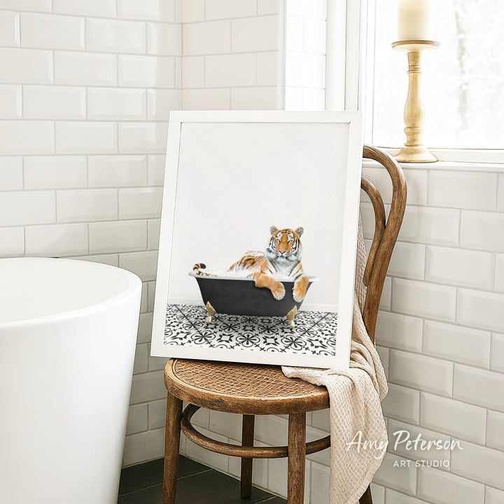 A framed image of a tiger sitting in a bathtub, with a towel draped over the back of a chair in a bathroom setting.