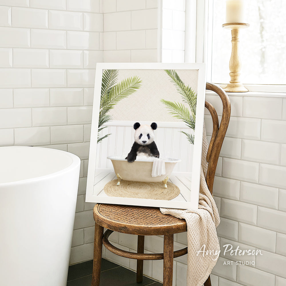 A framed image of a panda sitting in a bathtub, surrounded by palm leaves, is displayed on a wooden chair in a bathroom setting.