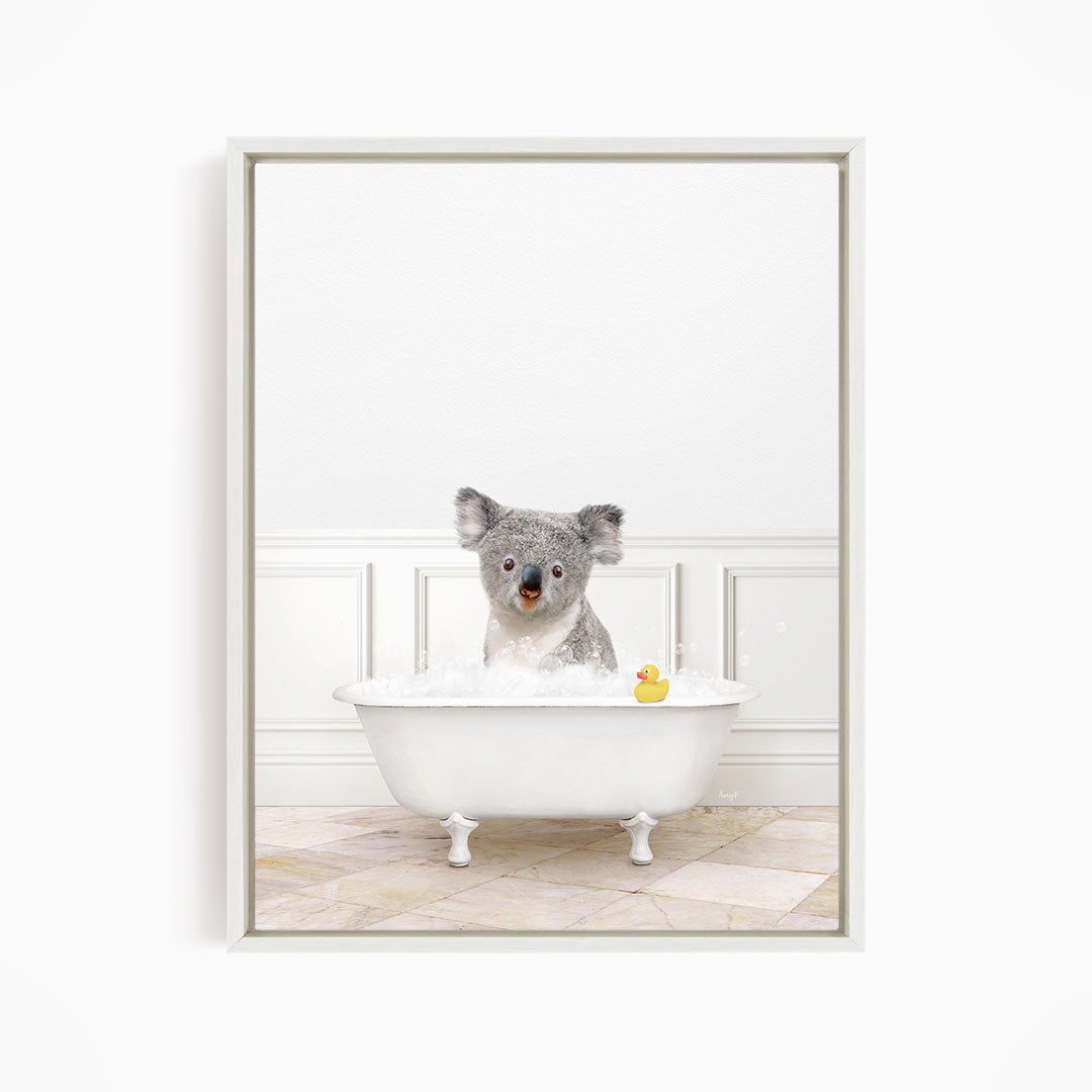 A koala bear sitting in a white bathtub, with a rubber duck floating in the water.