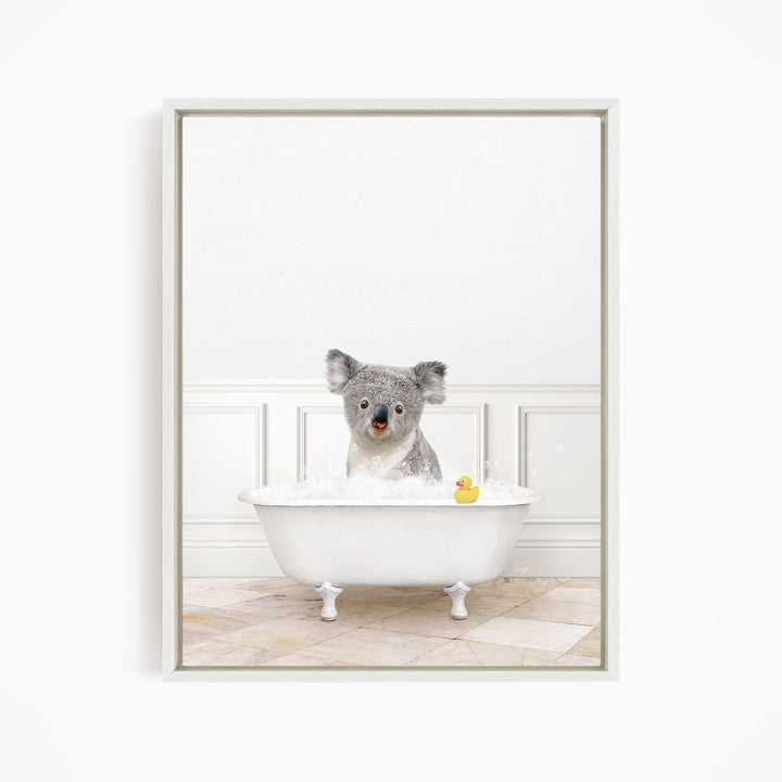 A koala bear sitting in a white bathtub, with a rubber duck floating in the water.