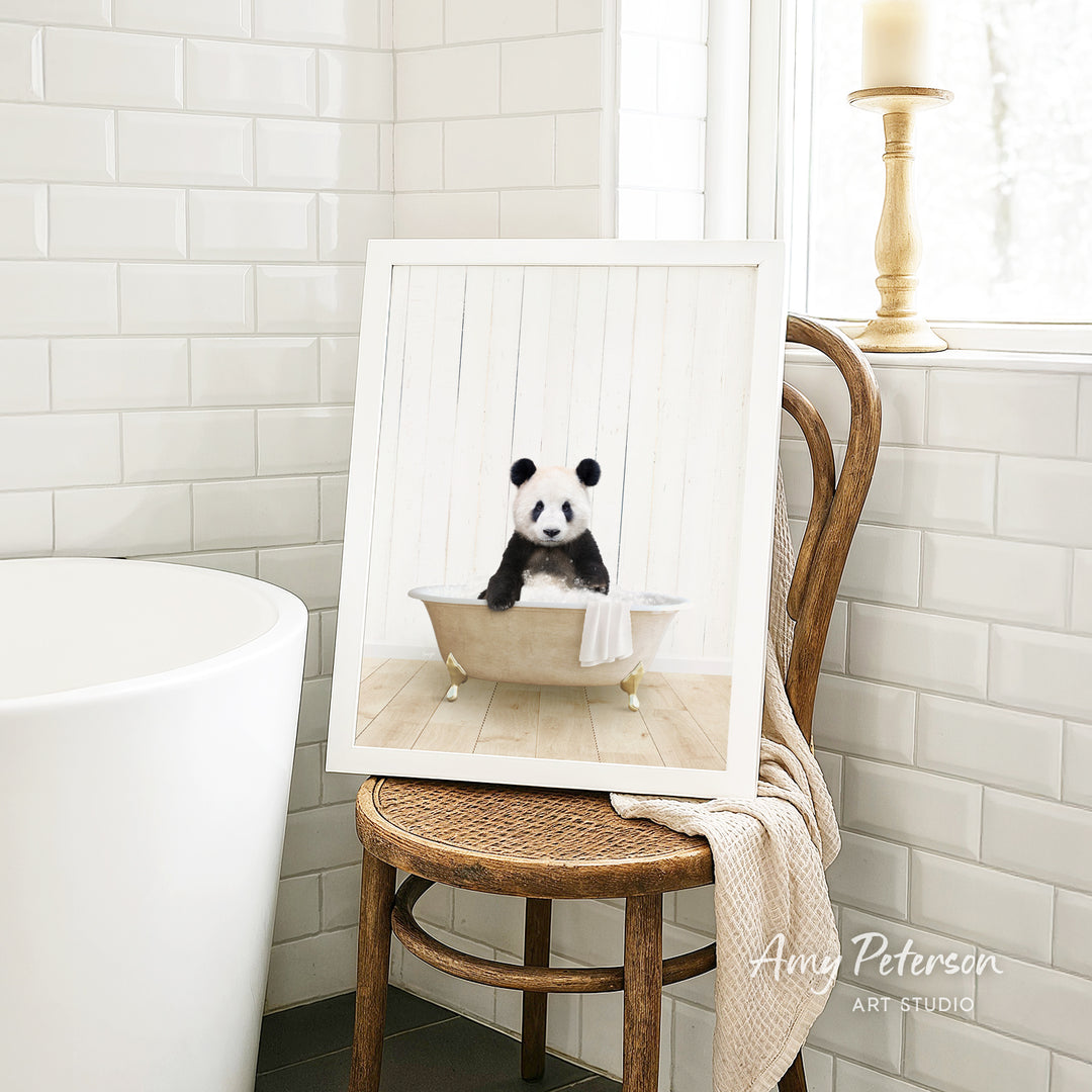 A framed image of a panda bear sitting in a bathtub is displayed on a wooden chair in a bathroom setting.