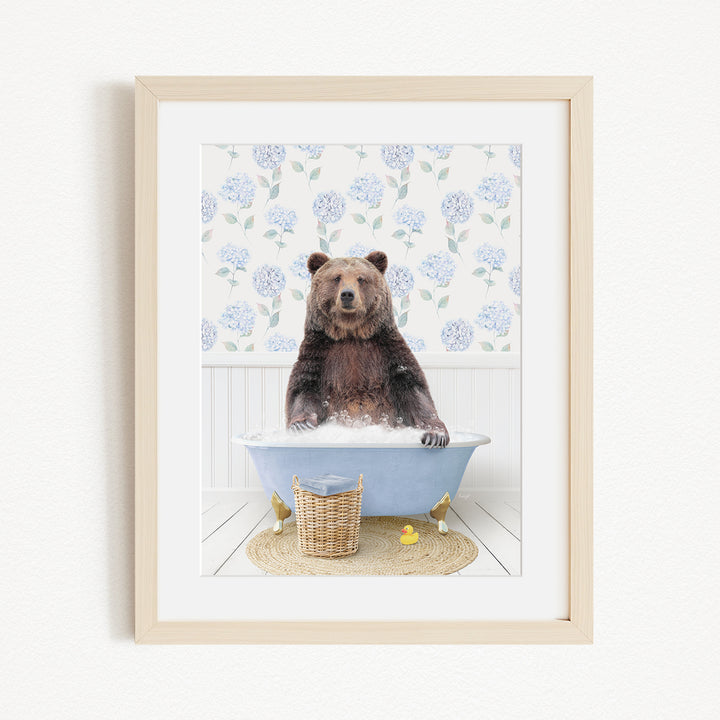 A brown bear sitting in a blue bathtub filled with water, surrounded by a floral patterned wall and a basket of rubber ducks.