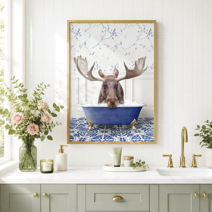 a framed picture of a moose sitting in a blue bathtub, surrounded by a floral pattern. The moose has large antlers and is partially submerged in the water. The picture is hung on a wall above a bathroom counter with various toiletries and decorative items.