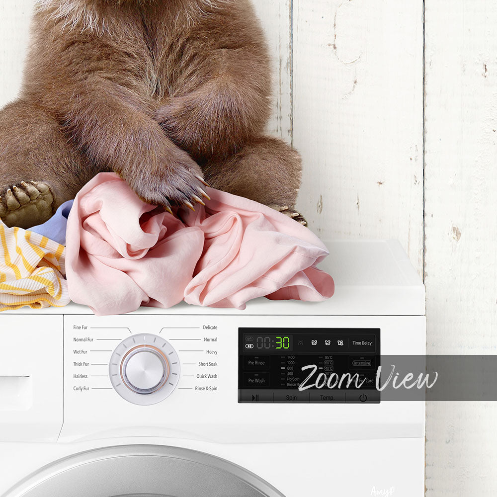 A brown bear sitting on top of a pile of clothes next to a washing machine.