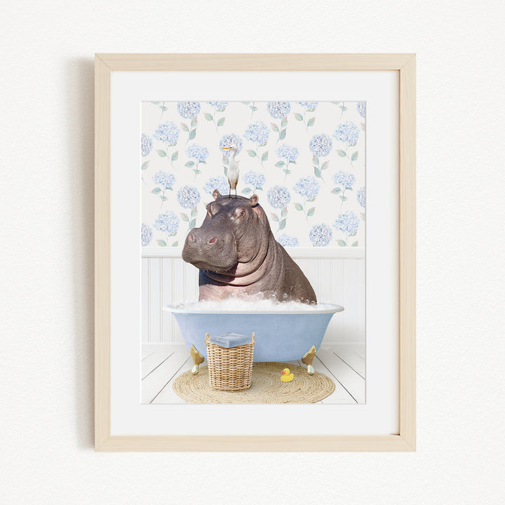 A framed image depicting a hippopotamus sitting in a bathtub filled with bubbles, surrounded by a blue floral patterned wall and a basket of rubber ducks.