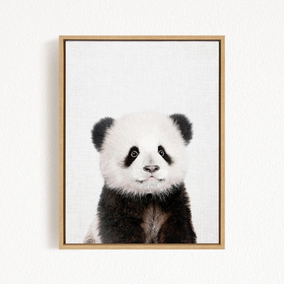 A panda bear with black and white fur is the focus of the image, which is a framed print hanging on a white wall.