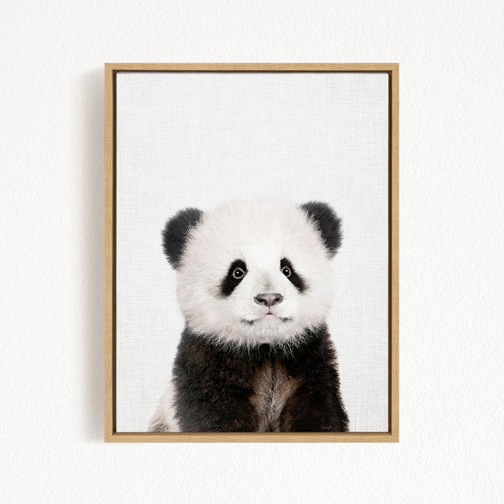 A panda bear with black and white fur is the focus of the image, which is a framed print hanging on a white wall.
