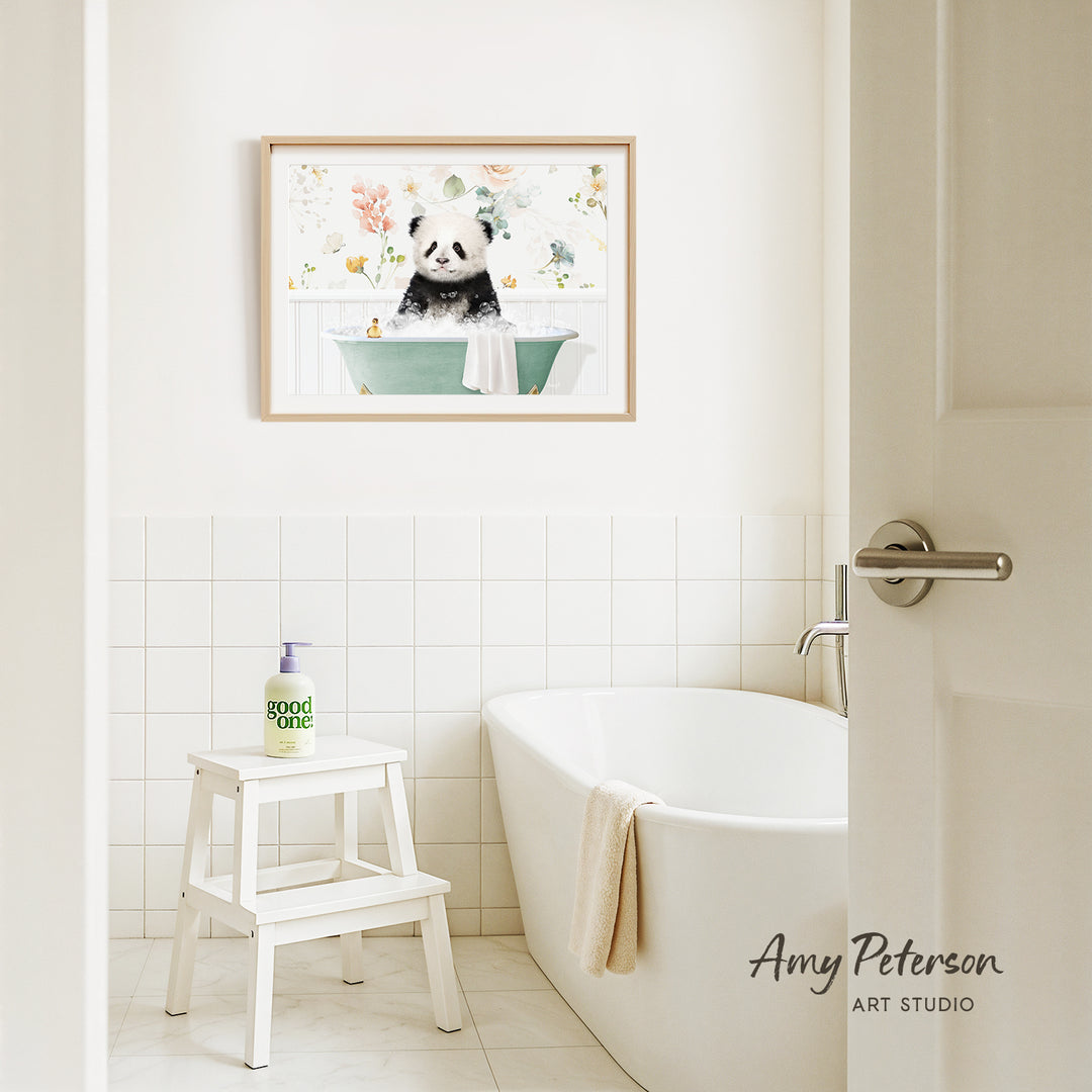 A framed painting of a panda sitting in a bathtub is hanging on a white tiled wall above a white bathtub in a bathroom.