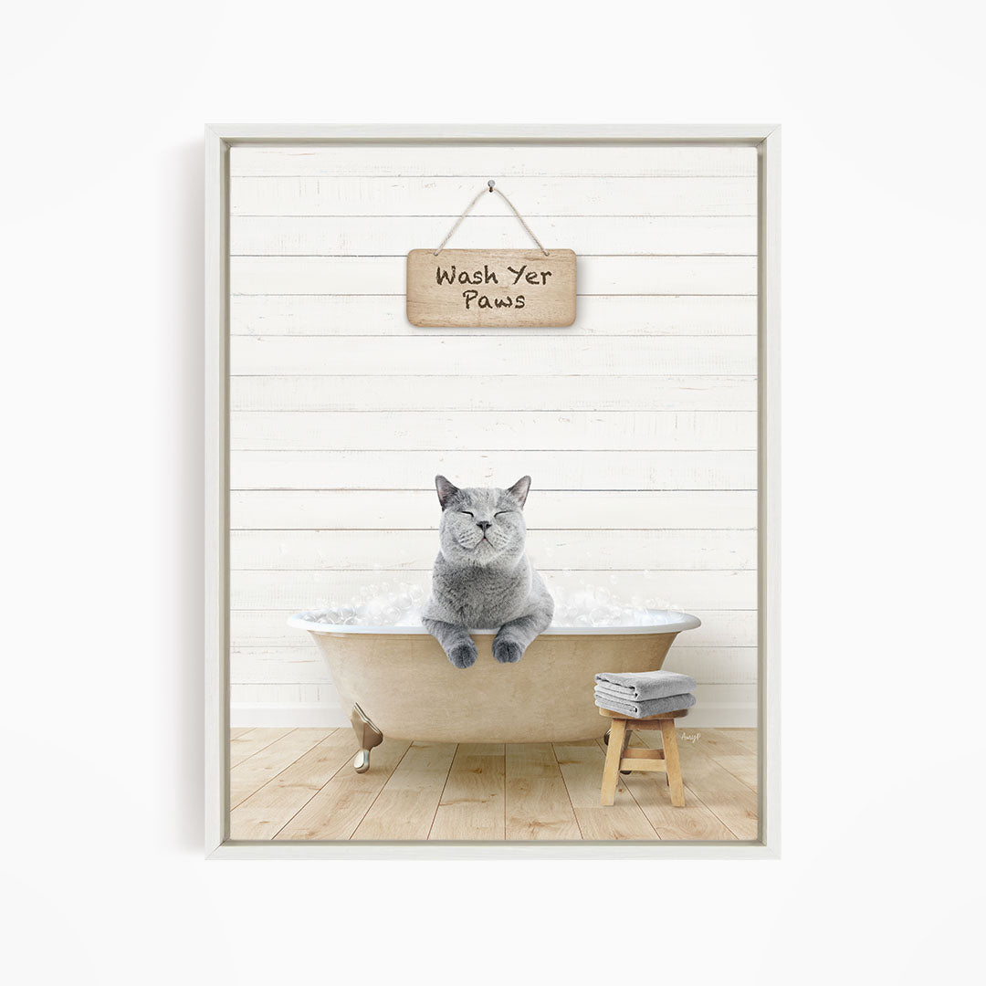 A gray cat sitting in a bathtub filled with bubbles, with a sign above that says "Wash Your Paws".