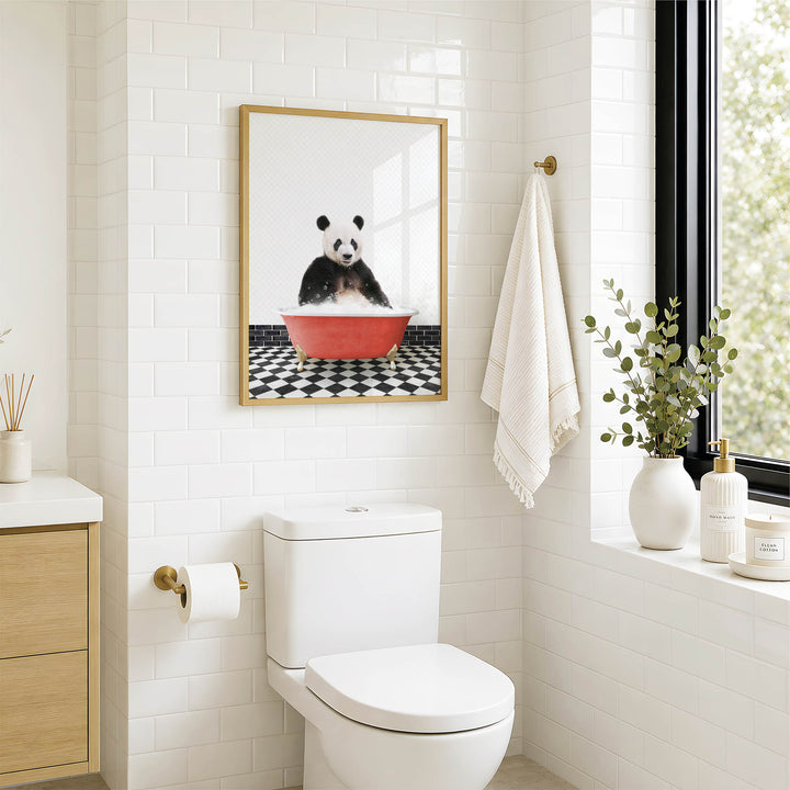 A bathroom with a white toilet, a framed picture of a panda sitting in a red bathtub, and a window with greenery outside.