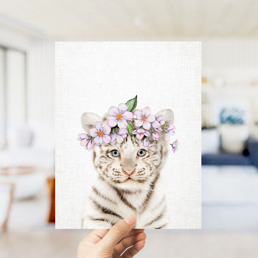 A hand is holding up a framed print of a tiger wearing a flower crown.