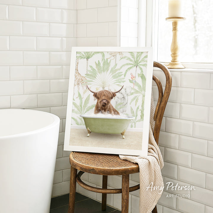 A framed image of a Highland cow sitting in a bathtub, surrounded by tropical foliage, is displayed on a wooden chair in a bathroom setting.