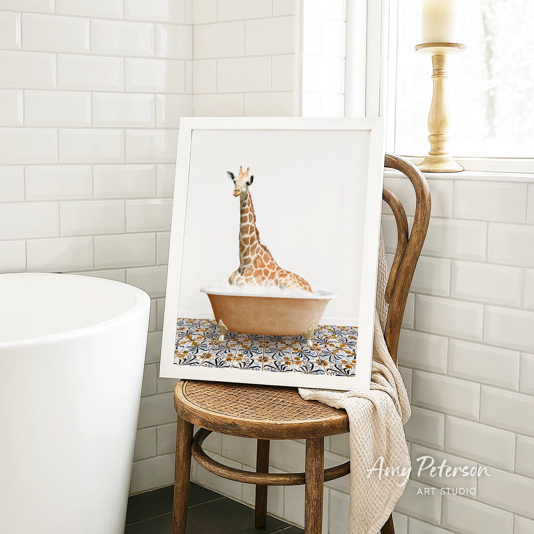 A framed image of a giraffe sitting in a bathtub is displayed on a wooden chair in a bathroom setting.