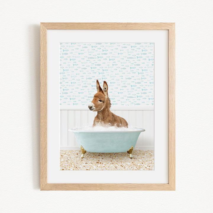 A donkey is sitting in a blue bathtub filled with bubbles, surrounded by a patterned wall and a wooden floor.