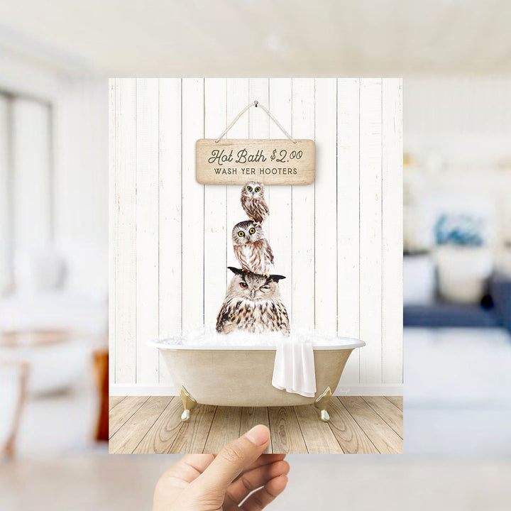 A hand holding a framed image of a wooden sign with a price list for hot baths, featuring a bathtub with three owls sitting in it.
