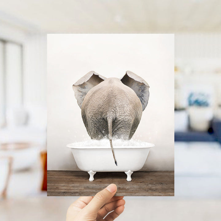 A hand holds up a framed image of an elephant standing in a bathtub filled with water, creating a whimsical and playful scene.