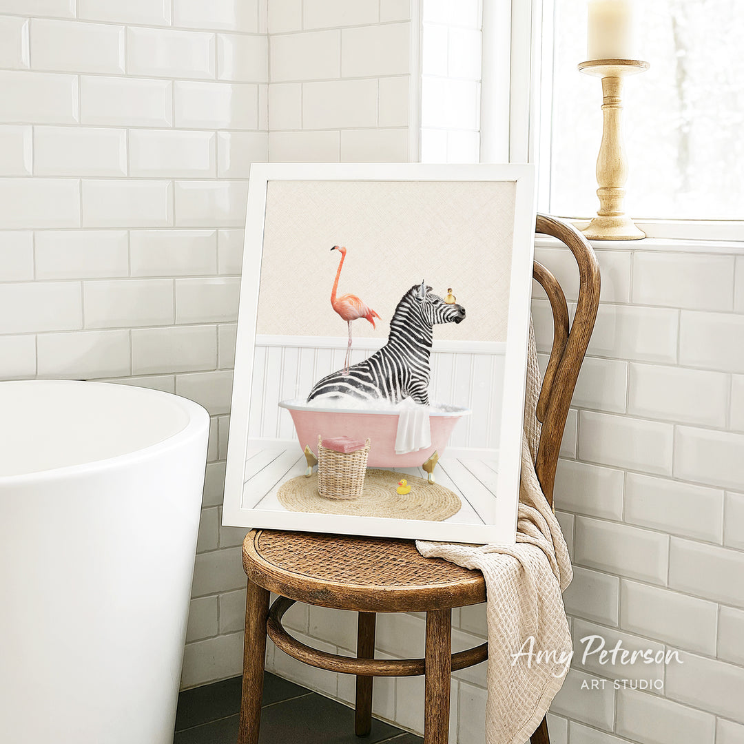 A framed illustration of a zebra sitting in a pink bathtub, with a pink flamingo standing on one leg next to it.
