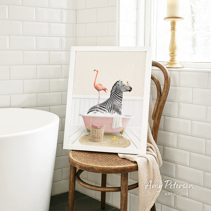 A framed illustration of a zebra sitting in a pink bathtub, with a pink flamingo standing on one leg next to it.