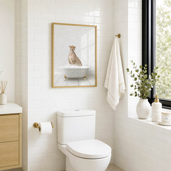 A bathroom with a white toilet, a framed picture of a cheetah sitting in a bathtub, and a window with greenery on the sill.
