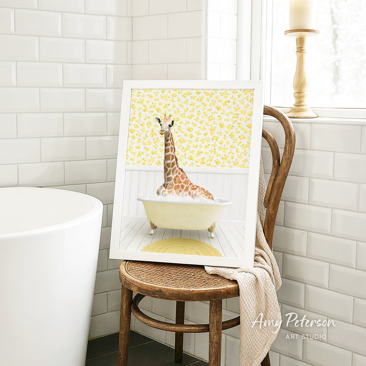 A framed image of a giraffe sitting in a bathtub, with a yellow floral pattern on the wall behind it.