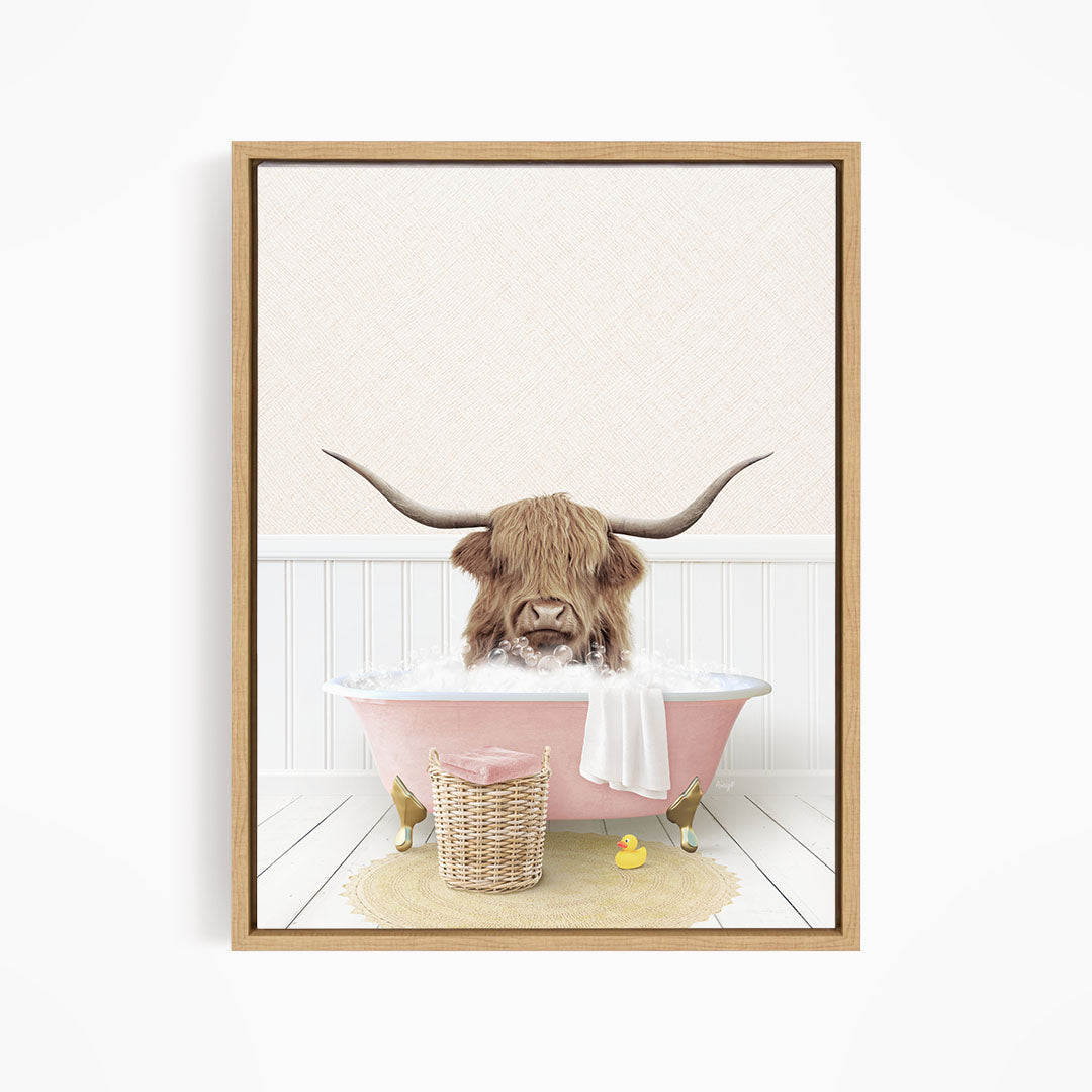 A brown cow with long horns is sitting in a pink bathtub filled with water, surrounded by a yellow rubber duck and a wicker basket.