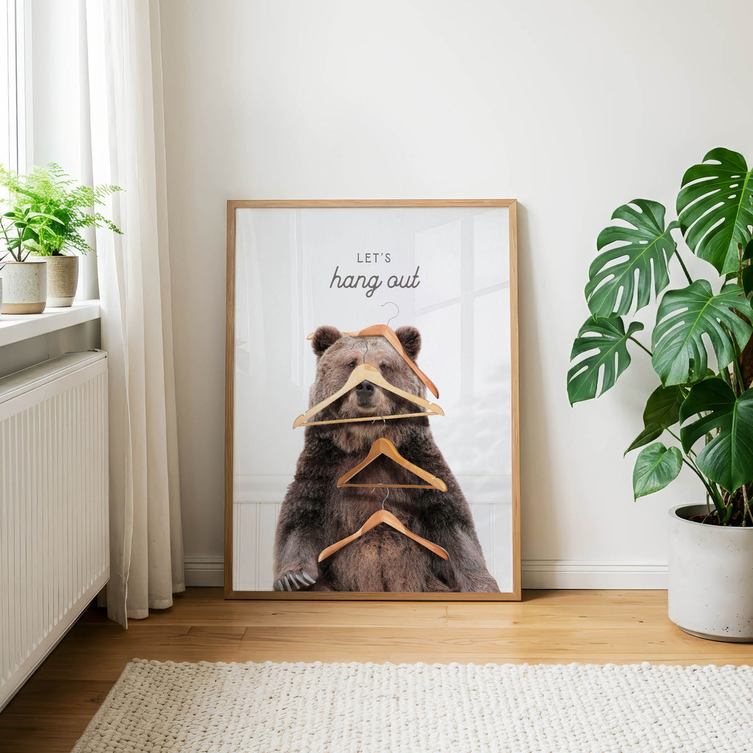 A framed poster with a bear sitting on a pile of hanging clothes, with the text "Let's hang out" written on it.