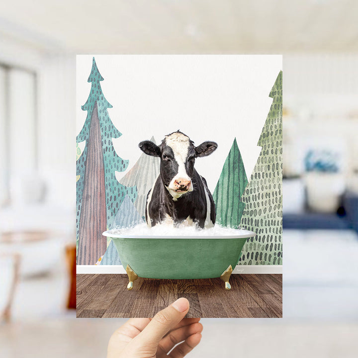 A black and white cow is sitting in a green bathtub, surrounded by trees and a snowy landscape.